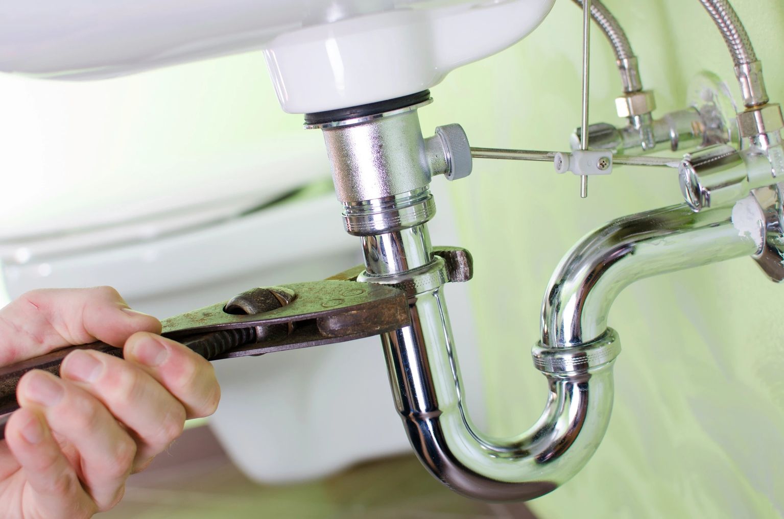 Hands tightening a chrome P-trap beneath a sink